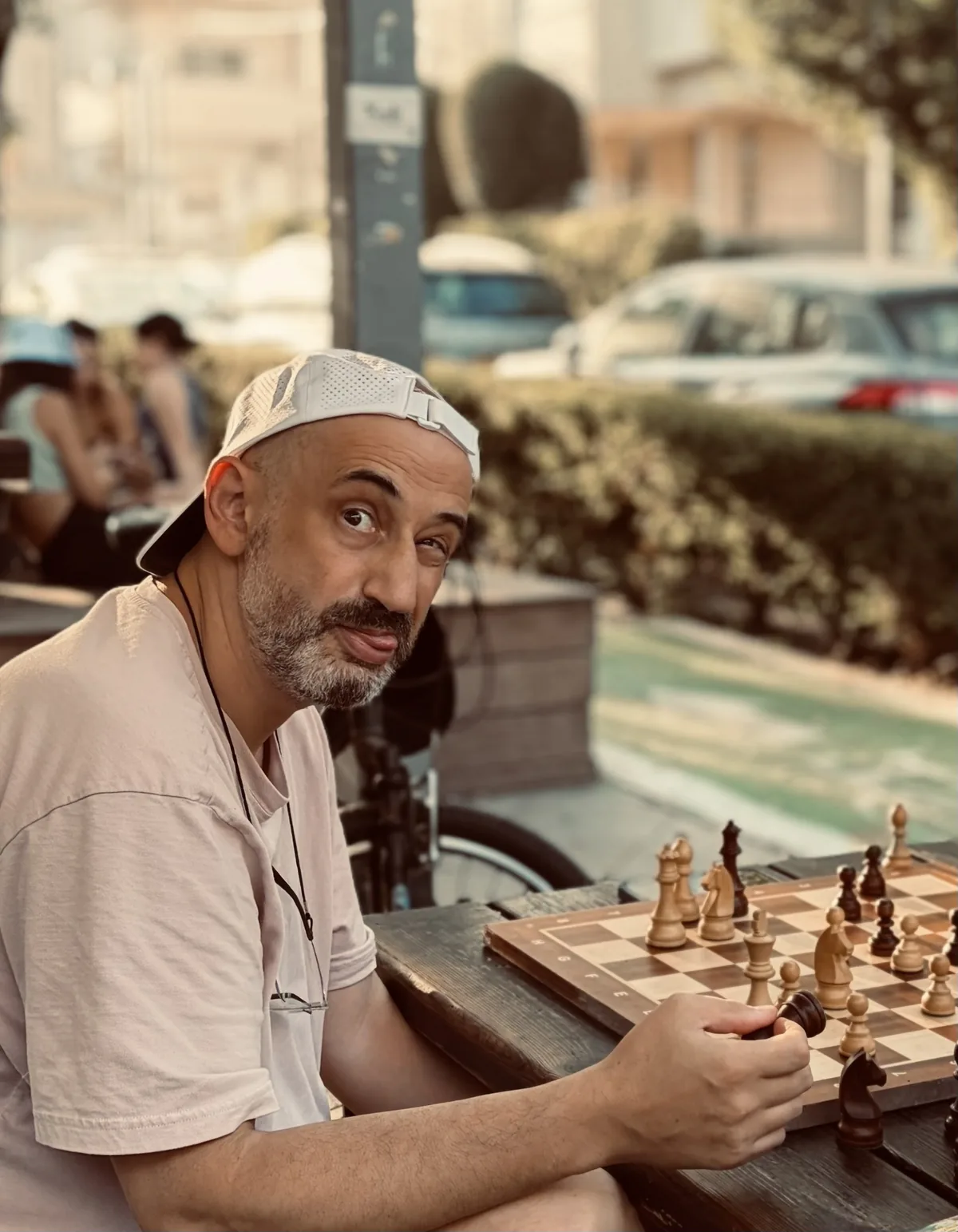 Mike Daykhin at a street chess table, a piece in his hand, looking up from the board